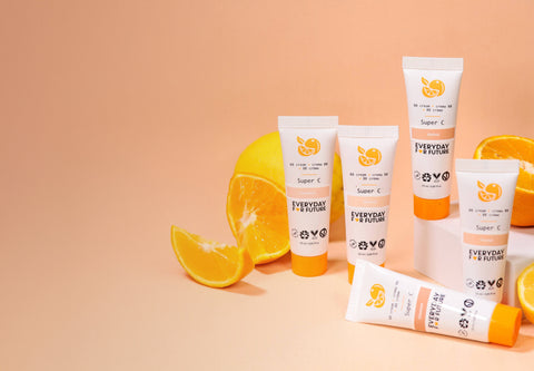 Multiple tubes of 'Everyday Super C' skincare product with orange slices on a peach background