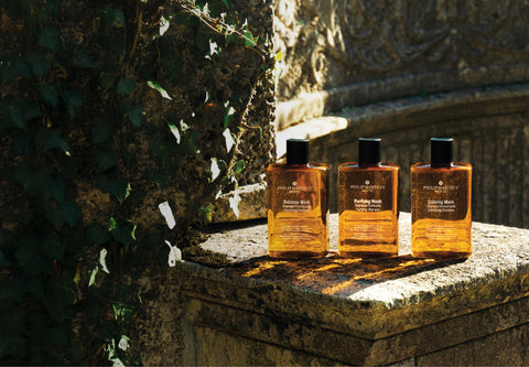 Three Philip Martin’s In Amber hair care bottles on a stone pedestal outdoors.