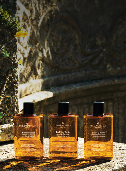 Three Philip Martin’s In Amber hair care bottles on a stone pedestal outdoors.